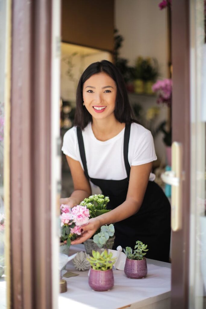 A cheerful florist arranges fresh flowers on a table inside a quaint flower shop.