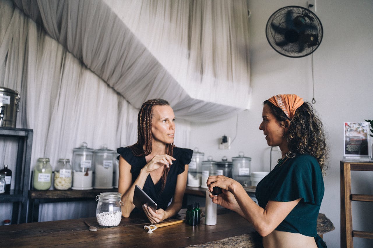 Two women engaging in conversation at an eco-friendly store with glass jars and refillable products.